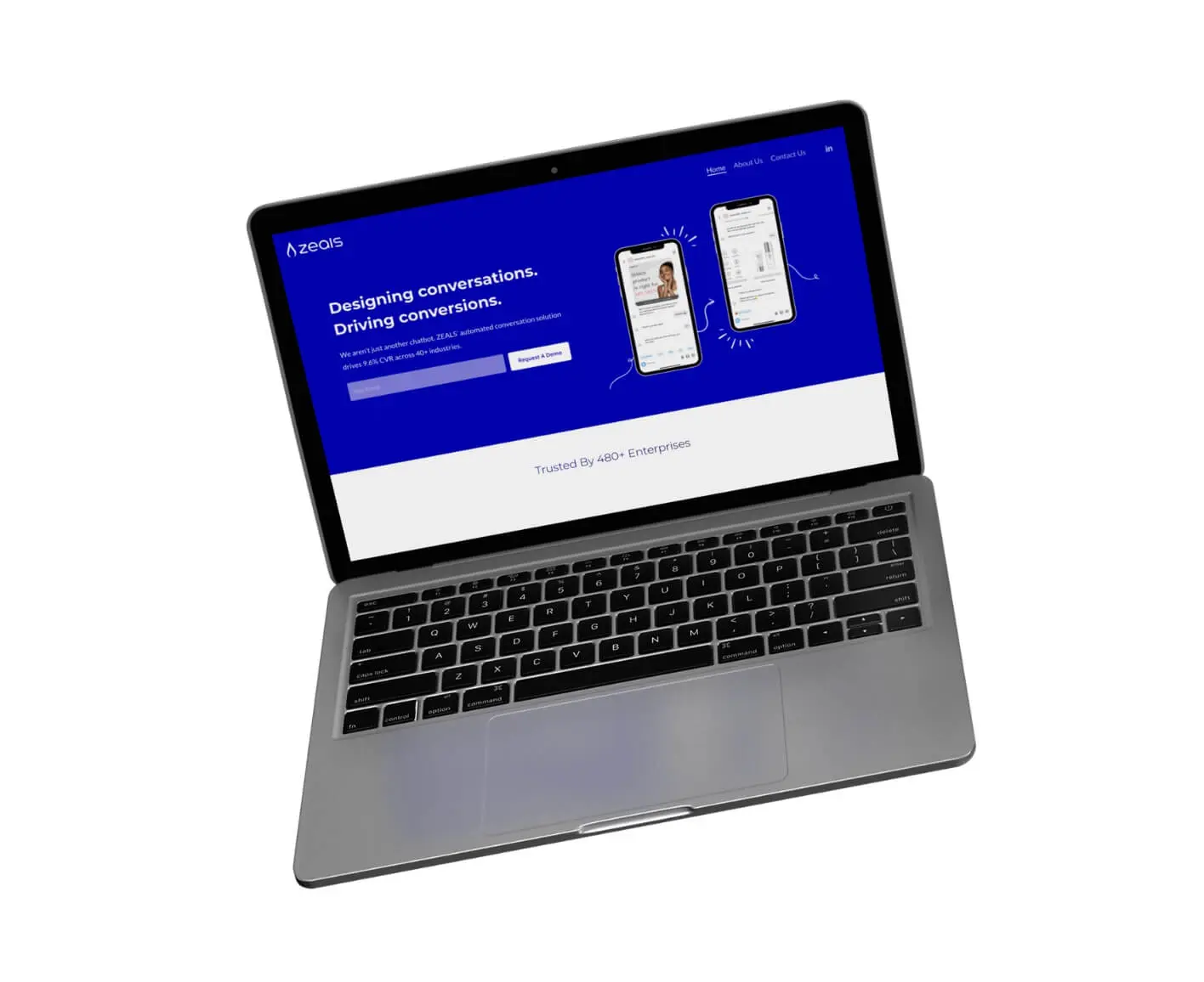 A silver laptop with a black keyboard displays a blue and white website homepage featuring chat interface graphics and the text “Designing conversations. Driving conversions.” on the screen.