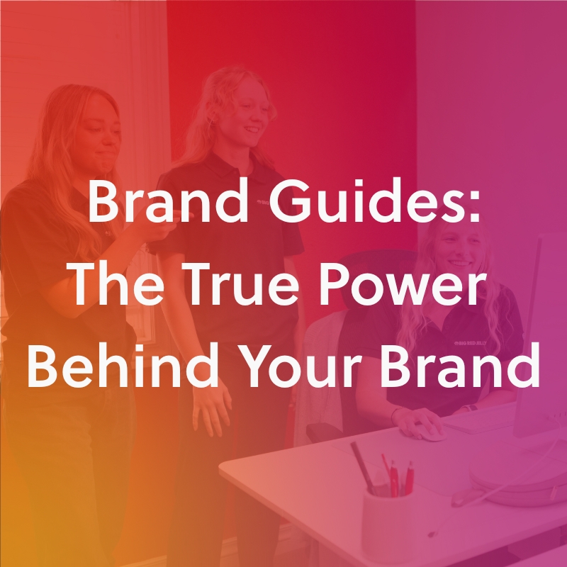 Three women in an office, two standing and one seated at a computer, with the text “Brand Guides: The True Power Behind Your Brand” overlaid on a red and orange gradient background.