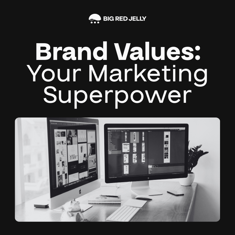 Black and white image with the text Brand Values: Your Marketing Superpower above two desktop computers on a desk, both displaying digital content. The logo Big Red Jelly appears at the top, hinting at what are brand pillars in effective marketing.