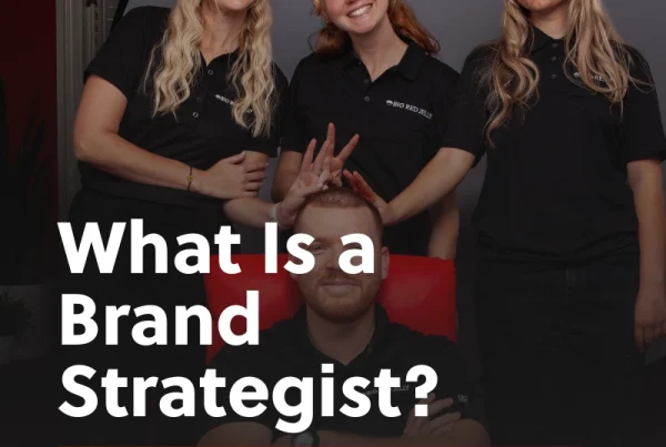 Four smiling people in black shirts pose together, with one seated and three standing behind. The text reads: What Is a Brand Strategist? Complete Career Guide to brand experience marketing.