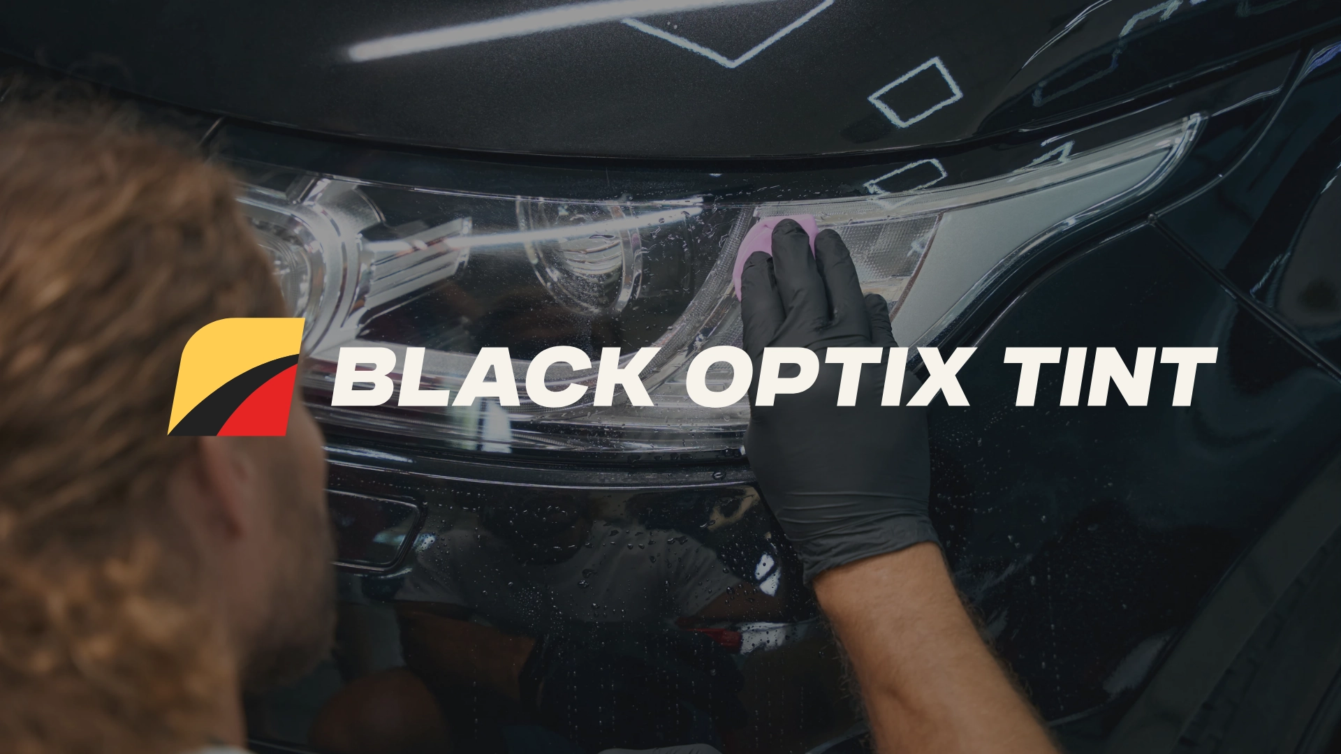 A person wearing black gloves cleans the headlight of a black car. The text BLACK OPTIX TINT is displayed across the image, with a colorful logo to the left of the text.