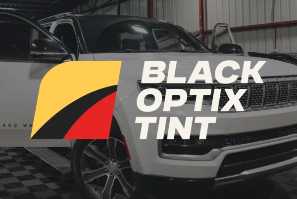 A white SUV inside a garage with the Black Optix Tint logo and text, featuring yellow, black, and red shapes that highlight the Primal Basics of bold automotive style.