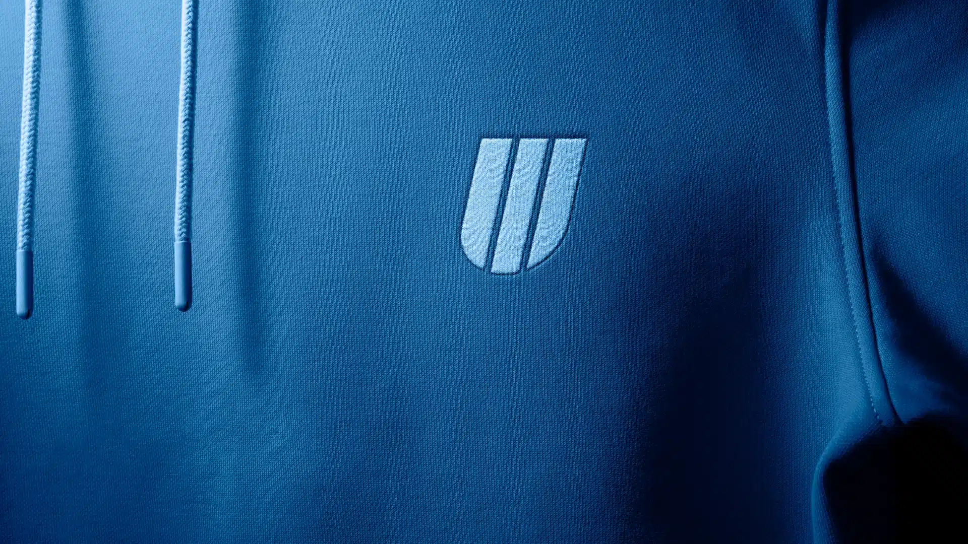 Close-up of a blue hoodie featuring a minimalist emblem with three vertical stripes on the chest and two drawstrings hanging down the left side.
