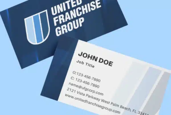Three business cards on a light blue background display the United Franchise Group’s blue and white shield logo, along with contact details for John Doe, including phone number, email, address, and website.