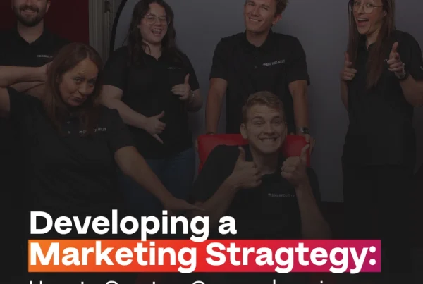 Five smiling people pose in front of a backdrop, with some giving thumbs up. Text on the image reads: Developing a Marketing Strategy: How to Create a Comprehensive Plan That Actually Works Long-Term.